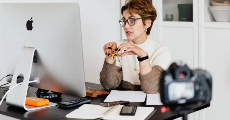 A professional woman engaged in a virtual meeting setup at her home desk, using a computer and camera.